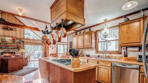 A spacious kitchen with wooden cabinets, a central island, and hanging pots. - The Bird House Stay - Firepit and Grill (Dillard)
