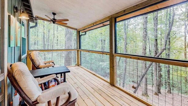 A covered outdoor seating area with a table and chairs, large windows, and a ceiling fan. - White Pine Perch Stay (Clayton)