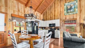 Interno di una baita di legno con zona pranzo, cucina e soggiorno.