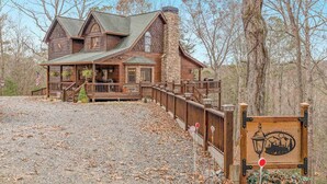 A rustic log cabin with a stone chimney, wooden deck, and a gravel driveway. - Copper Lantern Stays (Ellijay)