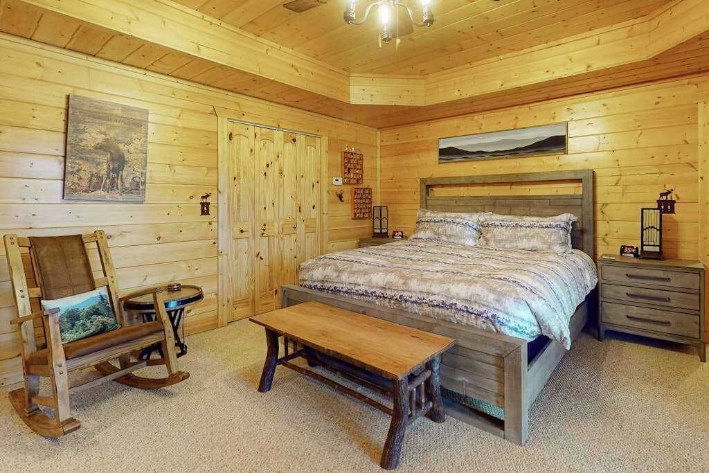 A wooden cabin bedroom with a bed, bench, dresser, and a rocking chair.