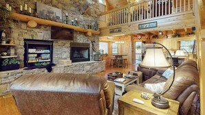 A spacious living room with a stone fireplace, leather furniture, and a wooden ceiling. - Copper Lantern Stays (Ellijay)