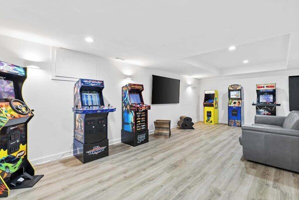 Ein Zimmer mit Spielautomaten, einem grauen Sofa und einem flachbildfernseher an der Wand.