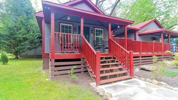 A two-story cabin with a red exterior, a porch with steps, and a stone pathway leading to the entrance.