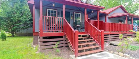 A two-story cabin with a red exterior, a porch with steps, and a stone pathway leading to the entrance.