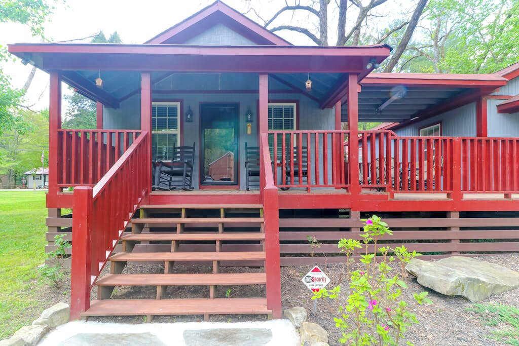 A red wooden house with a porch, steps, and a security sign.