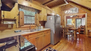 A wooden cabin interior with a kitchen, dining area, and a large window. - Swiss Puure Huus Cabin (Blue Ridge)