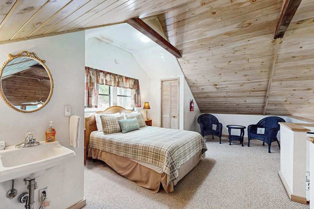 Un dormitorio con cama, espejo, lavabo y ventana con cortinas.