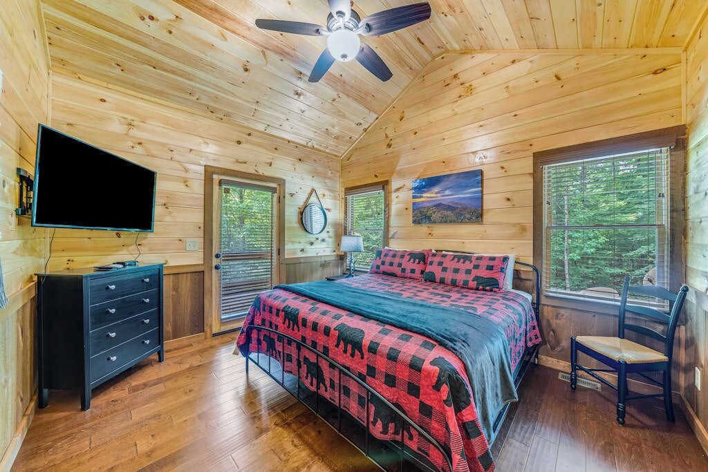 A wooden cabin bedroom with a bed, a TV, a dresser, and a chair.