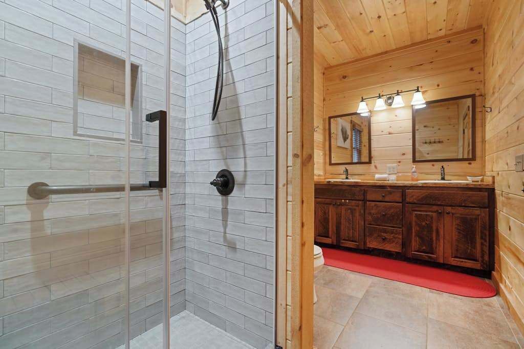 Une salle de bain avec une douche à parois de verre, des meubles en bois et un tapis de bain rouge.