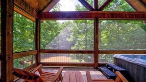 Eine Holzhütte mit Whirlpool, einer Holzdiele und Blick auf den Wald.