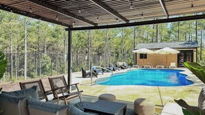 Uma área externa coberta com piscina, espreguiçadeiras e um pequeno edifício.