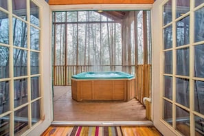 Tinaja de madera en una terraza con puertas de vidrio, rodeada por un bosque.
