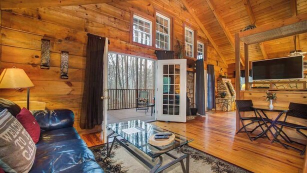A log cabin interior with a leather sofa, a glass coffee table, a TV, and a dining area.