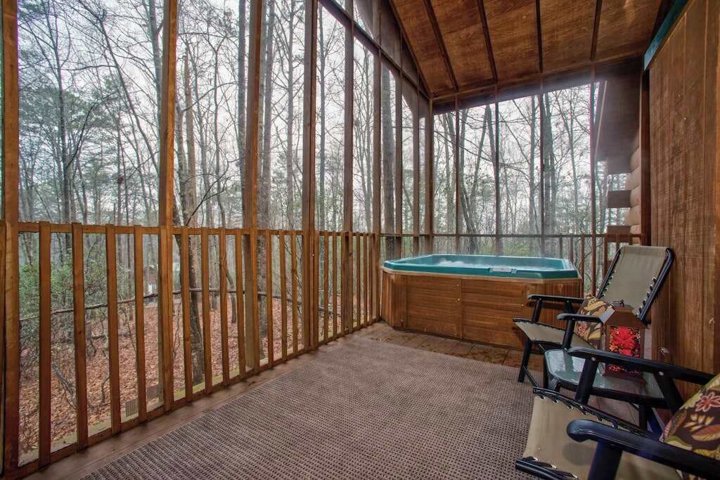 A wooden deck with a hot tub, chairs, and a view of a forest.