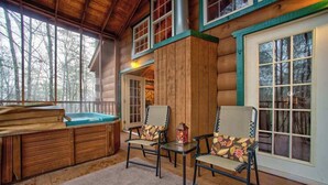A log cabin with a hot tub, two chairs, and a view of trees.