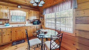 Een houten chalet van binnen, met een keuken, eethoek en grote ramen.