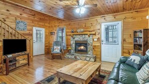 Ein Blockhaus-Interieur mit Kamin aus Naturstein, einem Fernseher, einem Ledersofa und einem Deckenventilator.