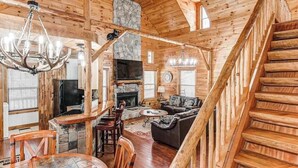 A log cabin interior with a stone fireplace, wooden staircase, and a cozy living area. - Wooded Wonder Retreat (Cleveland)