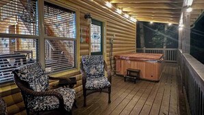 A wooden deck with two patterned chairs, a hot tub, and a view of a forested area. - Wooded Wonder Retreat (Cleveland)