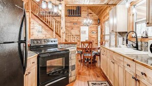 A wooden cabin interior with a kitchen, dining area, and staircase. - Wooded Wonder Retreat (Cleveland)
