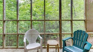 A room with a large window, a white plastic chair, a wooden stool, and a green Adirondack chair.
