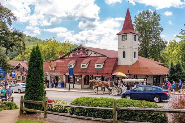 A traditional building with a red roof and a tower, surrounded by greenery and a street with pedestrians and a horse-drawn carriage.