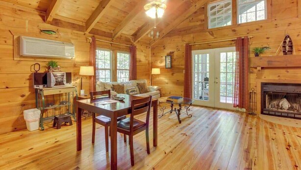 A log cabin interior with a dining area, a fireplace, and a large window.