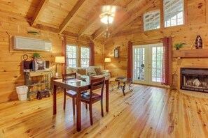 A log cabin interior with a dining area, a fireplace, and a large window.