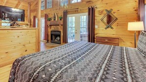 A log cabin bedroom with a bed, fireplace, television, and a ceiling fan.
