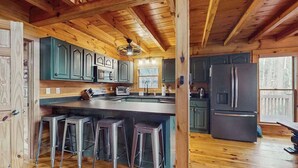 L’intérieur d’un chalet en bois comprend une cuisine avec des meubles verts, un grand îlot central doté de tabourets et un réfrigérateur.