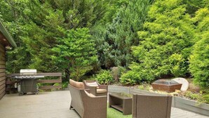 Una terrassa amb mobles de vimet, una barbacoa i un jardí amb vegetació abundant.