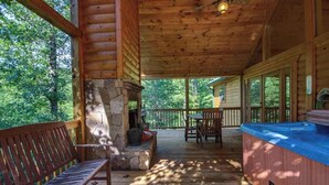 Une terrasse en bois avec une cheminée en pierre, un jacuzzi et un banc.
