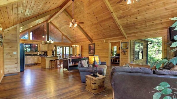 L’intérieur de cette vaste cabane en bois comprend un coin repas, une cuisine et un salon aménagé avec des canapés et une table basse.