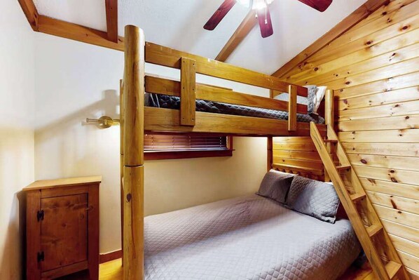 Un letto a castello con una scala, un piccolo armadietto in legno e un soffitto spiovente con travi in legno.