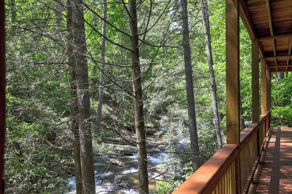 Une terrasse en bois donnant sur une zone boisée, avec un ruisseau.