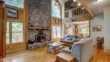 Un vaste espace de vie agrémenté d’une cheminée en pierre, de planchers en bois, d’une mezzanine avec balcon et de grandes fenêtres.