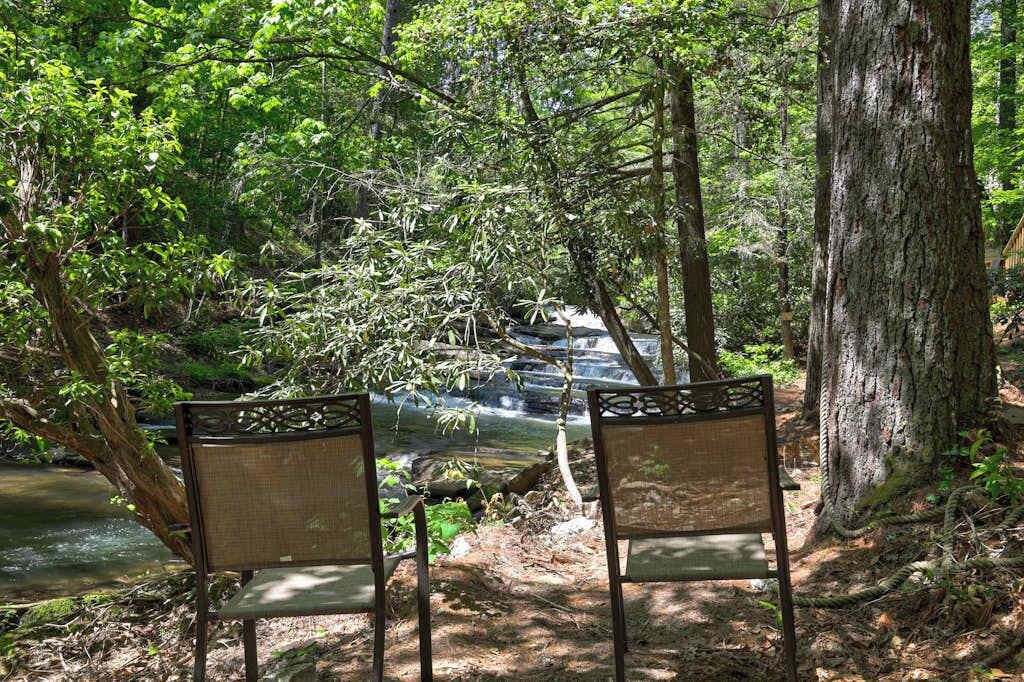 Twee houten stoelen gericht op een waterval in een bebost gebied.