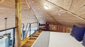 Une chambre mansardée en bois, avec un lit, un bureau et une chaise.