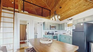 Une cuisine moderne avec un plafond en bois, des meubles de couleur bleu clair, un îlot central et un réfrigérateur noir.