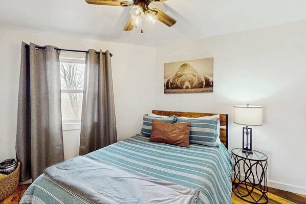 A bedroom with a bed, curtains, a ceiling fan, a bedside lamp, and a wall-mounted picture. - Valley Vista Getaway (Ranger)