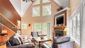 A spacious living room with leather sofas, a fireplace, a television, and large windows. - Alpine Retreat Stays (Helen)
