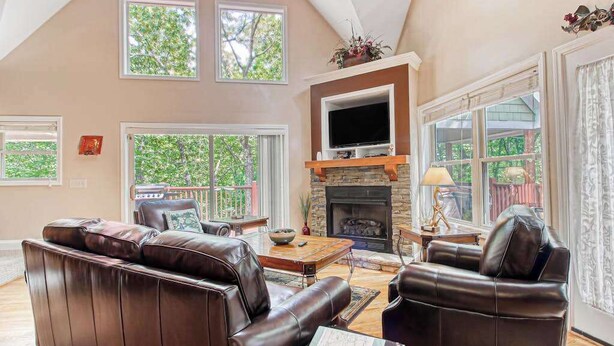 A spacious living room with a fireplace, leather sofas, and large windows. - Alpine Retreat Stays (Helen)