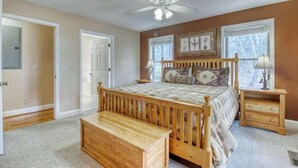A bedroom with a wooden bed, a bench, a nightstand, a ceiling fan, and framed artwork on the wall. - Alpine Retreat Stays (Helen)