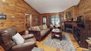Interior de uma cabana de madeira com sala de estar, lareira e cozinha.