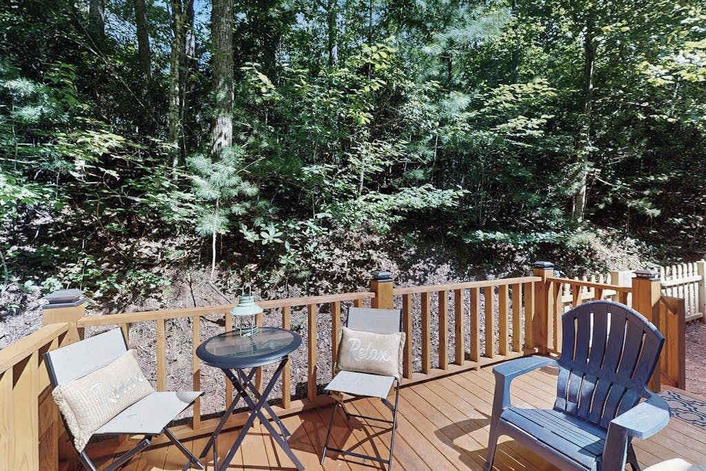 A deck with a table and chairs, surrounded by a wooden railing and dense forest.