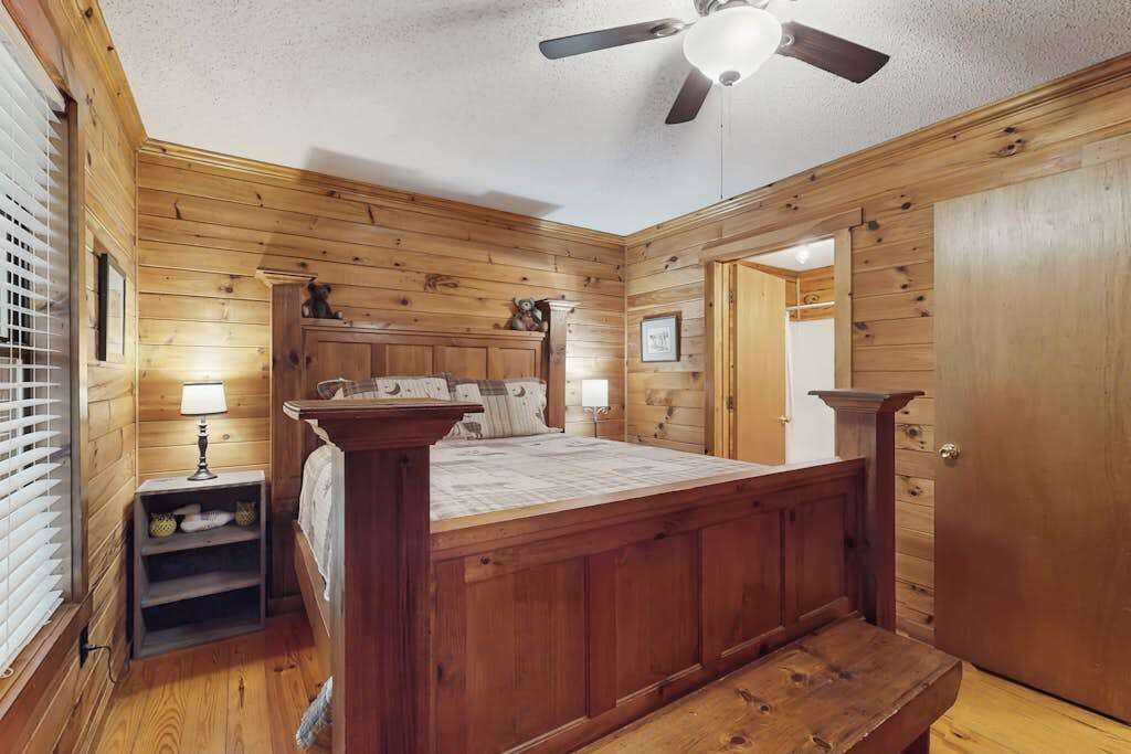 A wooden-paneled bedroom with a bed, bedside tables, a ceiling fan, and a door.