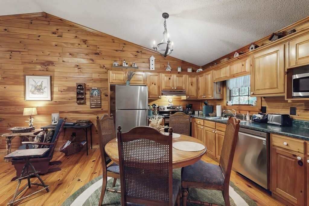 Interior de una cabaña de madera con una mesa de comedor, sillas, un refrigerador, un microondas y armarios de madera.