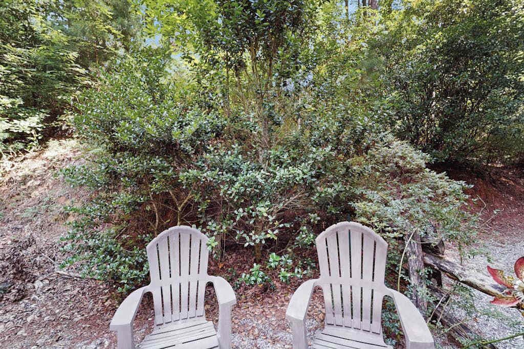 Dos sillas Adirondack mirando hacia una zona verde y tupida.