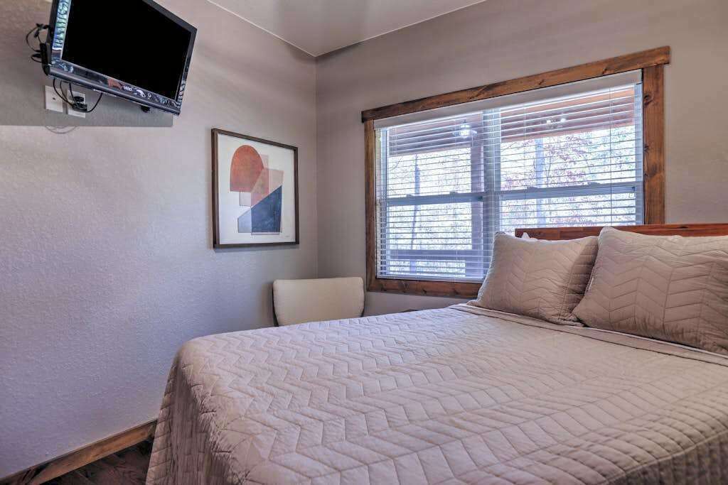 A bedroom with a bed, a chair, a window with blinds, and a television mounted on the wall.